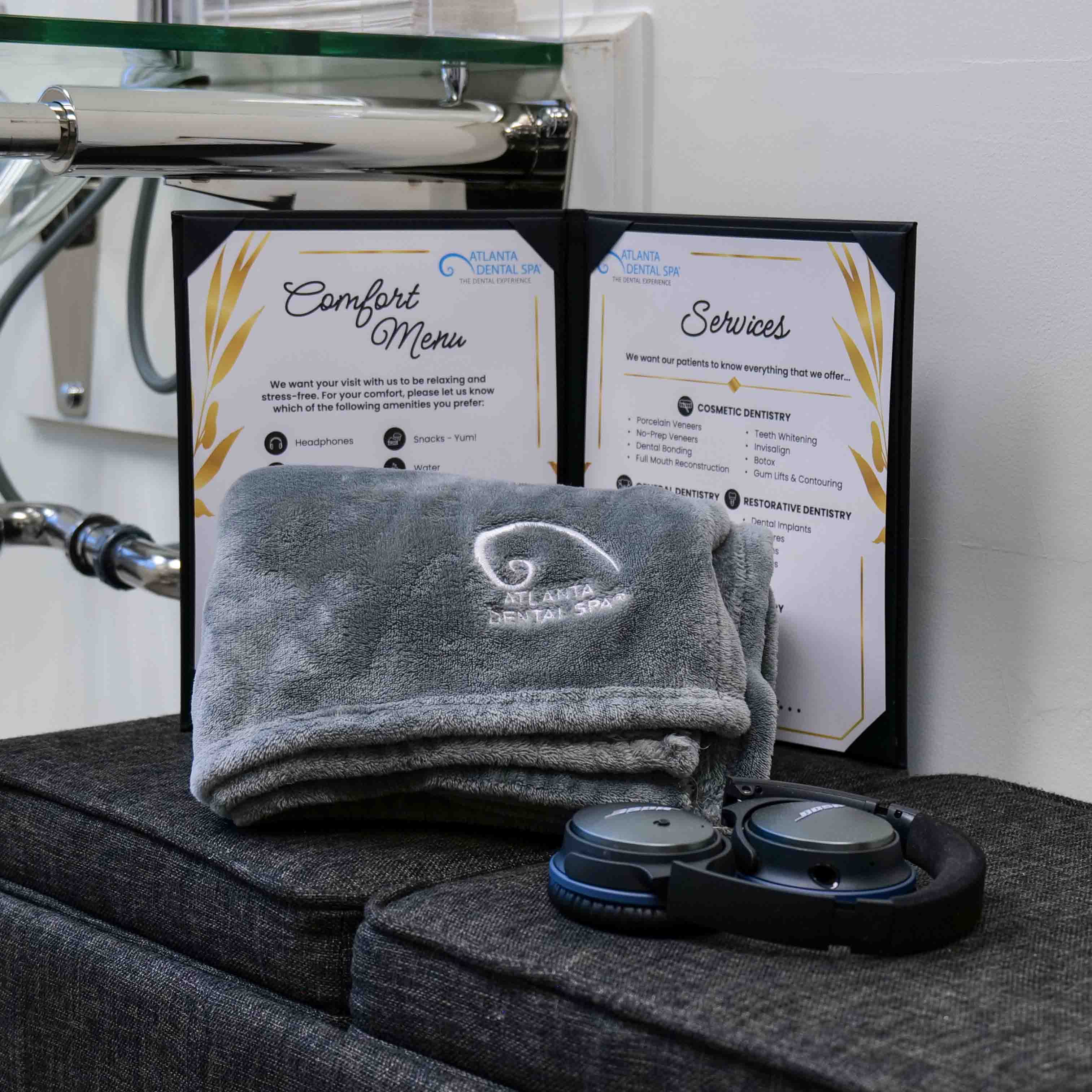 Atlanta Dental Spa Comfort Menu featuring cozy blankets embroidered with the logo, noise-canceling headphones, and a list of services for a relaxing dental experience.