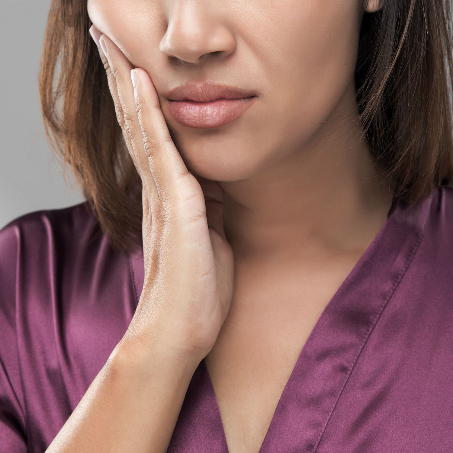 Woman holding her cheek in pain, possibly avoiding dental treatment due to no insurancel, highlighting the need for affordable dental care options.
